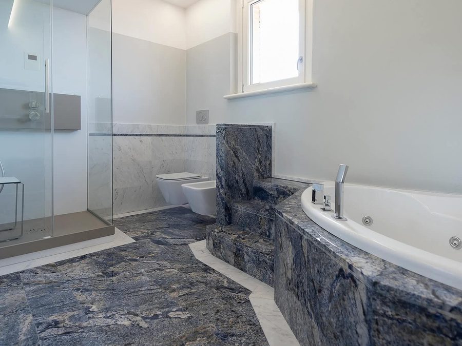 Bagno con vasca idromassaggio angolare e pavimento in pietra blu venata