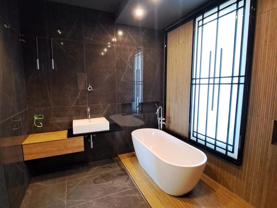 Bagno con vasca a centro stanza su pedana color legno e lastre scure effetto marmo