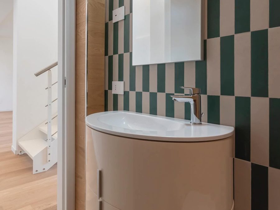 Bagno con piastrelle verdi e crema, mobile lavabo curvo e specchio